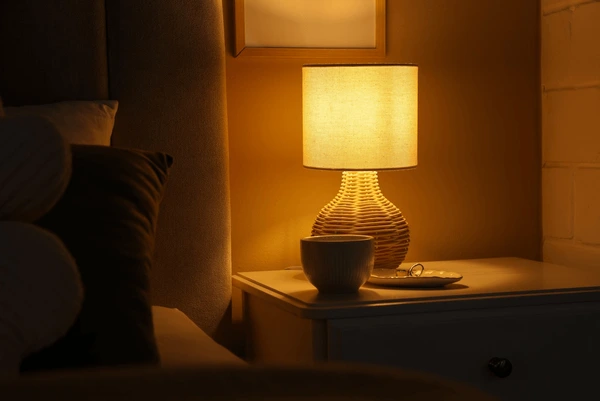 A warm bedside lamp glowing softly next to a folded blanket and a book